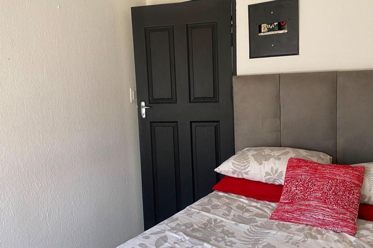 A bedroom interior featuring a dark painted door and an exposed electrical distribution board mounted on the wall.