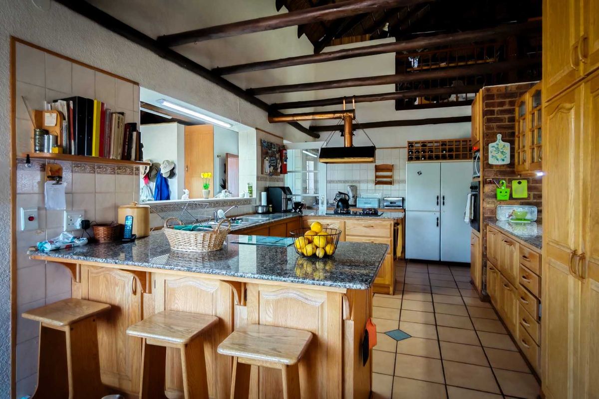 Spacious kitchen featuring granite countertops, wooden cabinetry, a breakfast bar, and exposed timber ceiling beams, offering a rustic and functional cooking space.