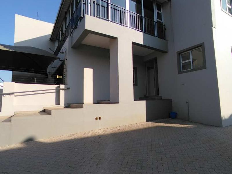 Modern multi-level residential facade featuring a paved driveway, upper-level balcony with metal railings, and clean architectural lines.