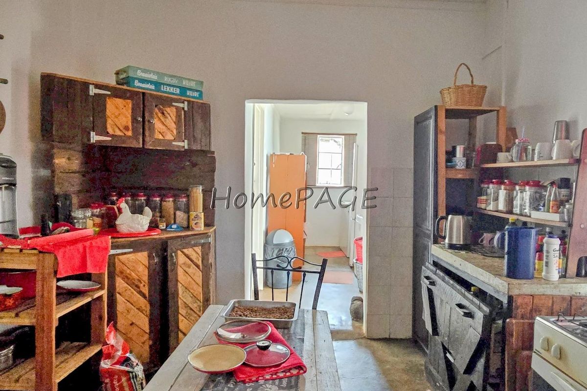 A rustic kitchen area featuring custom timber cabinetry and a functional layout, with an adjacent scullery or utility space visible through the doorway.