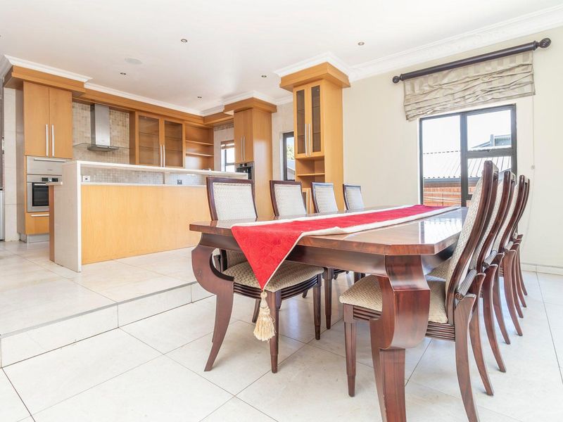 Open-plan kitchen and dining area featuring light wood cabinetry, built-in appliances, tiled flooring, and large windows providing natural light.