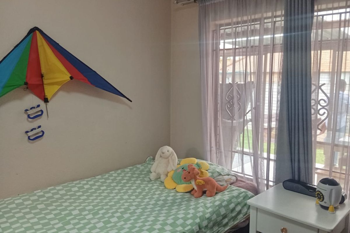 A bedroom featuring a large window with security bars and curtains, providing natural light and access to the exterior.