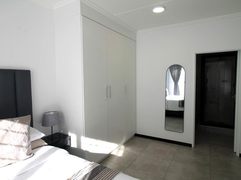 A clean, modern bedroom featuring neutral tiled flooring, a spacious built-in wardrobe, and direct access to an en-suite bathroom.