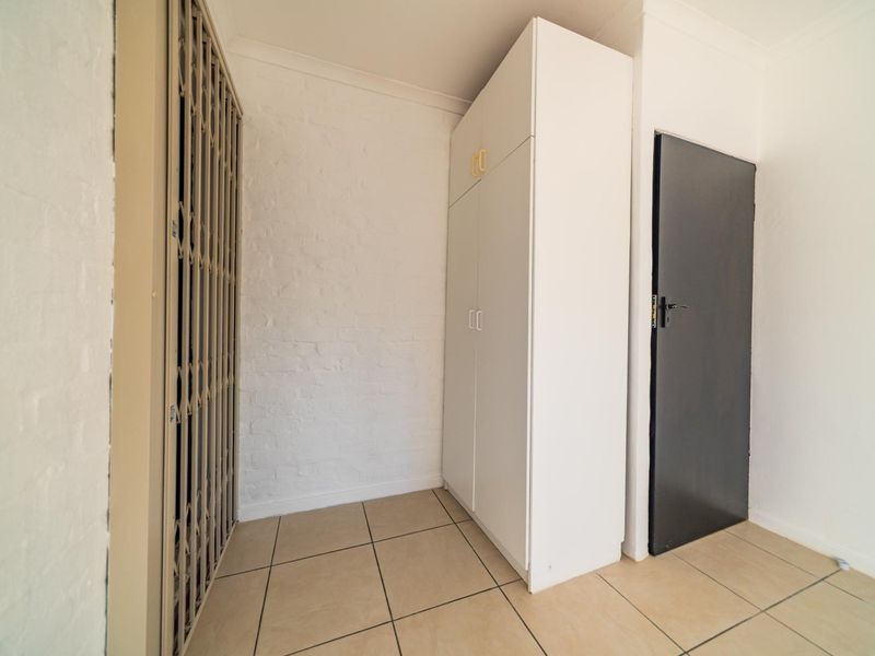 A clean, functional hallway featuring tiled flooring, a built-in storage cupboard, and a secure metal gate.