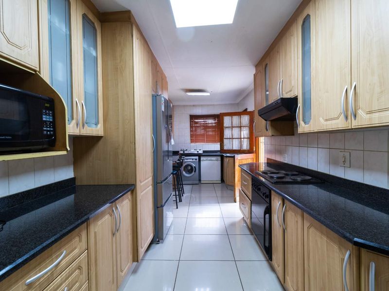 A galley-style kitchen featuring light wood cabinetry, dark granite countertops, tiled flooring, and a skylight, providing a functional and well-lit workspace.