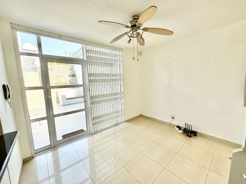 Bright and open living area featuring tiled flooring, a ceiling fan, and direct access to the outdoor patio through a secure glass sliding door.
