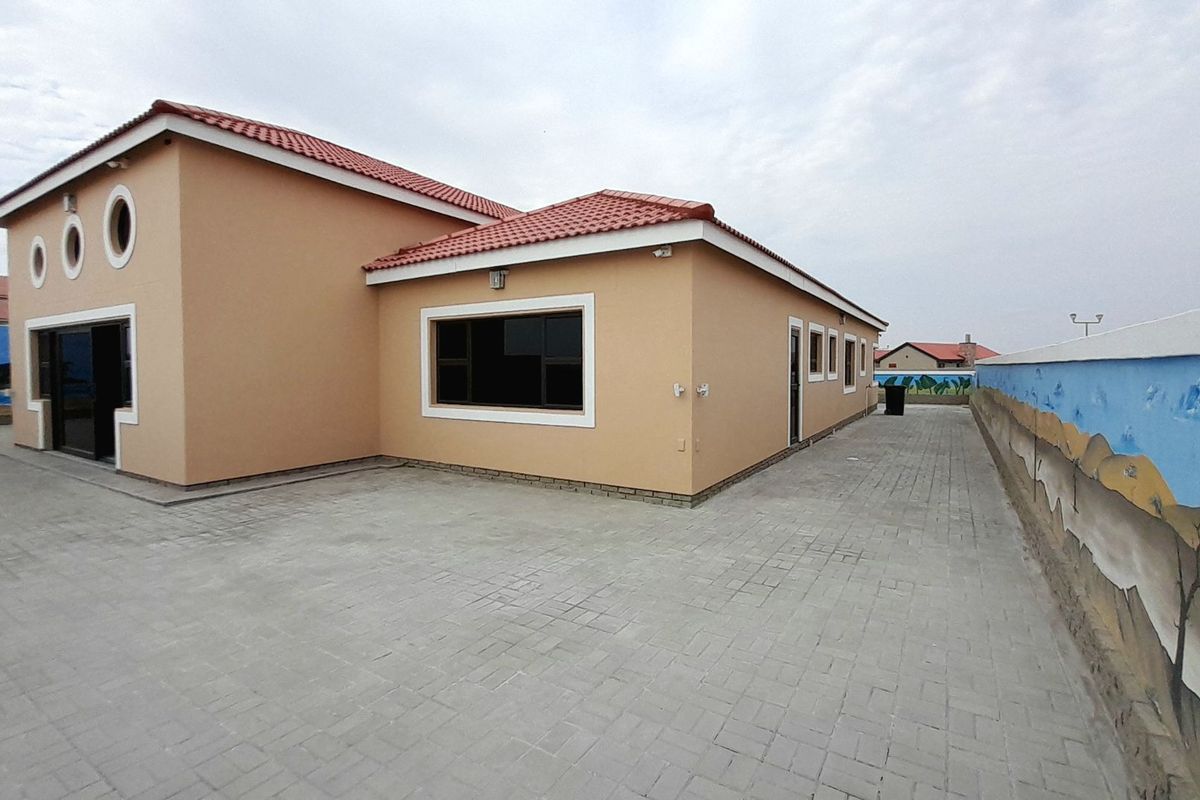Rear view of the property featuring a paved courtyard, tiled roof, and a painted boundary wall.
