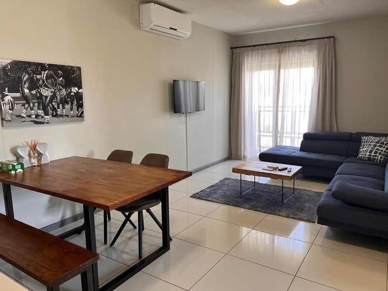 Open-plan living and dining area featuring tiled flooring, a wall-mounted air conditioning unit, and sliding glass doors leading to an outdoor space.