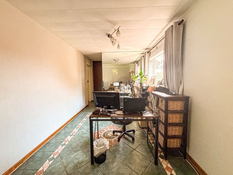 A functional office space featuring tiled flooring, track lighting, and a large wall mirror, providing a versatile area for work or study.