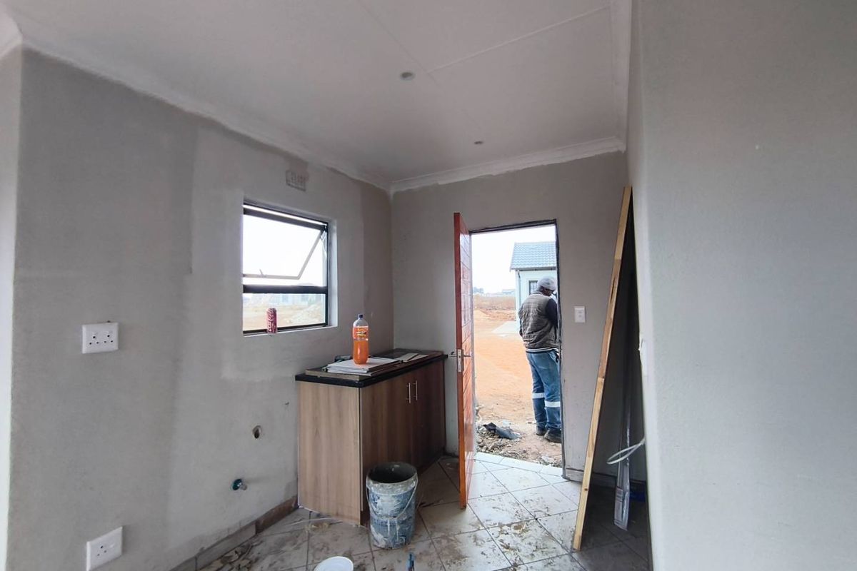 A small utility or kitchen area under construction, featuring a single base cabinet, tiled flooring, and direct access to the exterior.