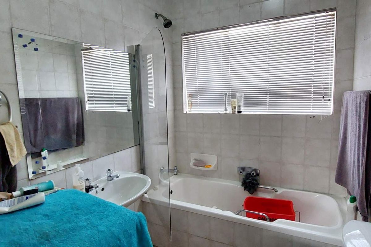 A functional bathroom featuring a bathtub with a glass shower screen, a wall-mounted basin, and full-height wall tiling.