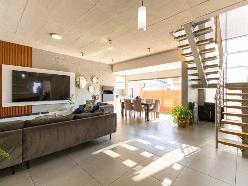 Spacious open-plan living and dining area featuring modern tiled floors, an exposed concrete ceiling, and a contemporary floating staircase with metal balustrades.