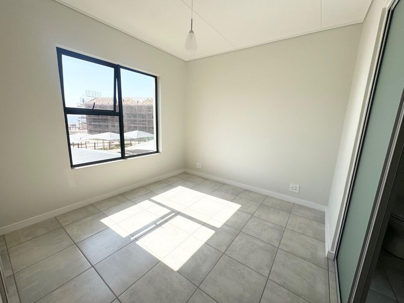 A bright, empty bedroom featuring neutral tiled flooring, modern aluminium window frames, and a built-in cupboard, ready for personalization.