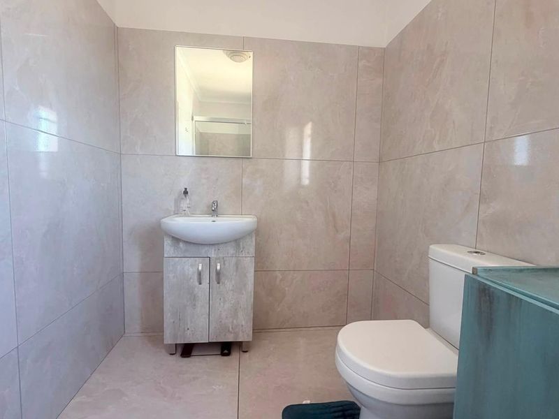 A clean, modern bathroom featuring neutral large-format wall and floor tiles, a vanity cabinet with a basin, and a wall-mounted mirror.