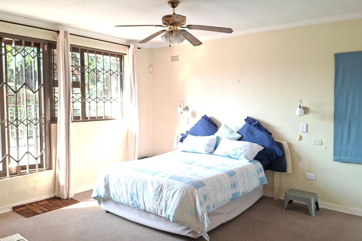 A spacious bedroom featuring a ceiling fan, security gates on windows, and wall-mounted lighting fixtures, offering a functional and comfortable living space.