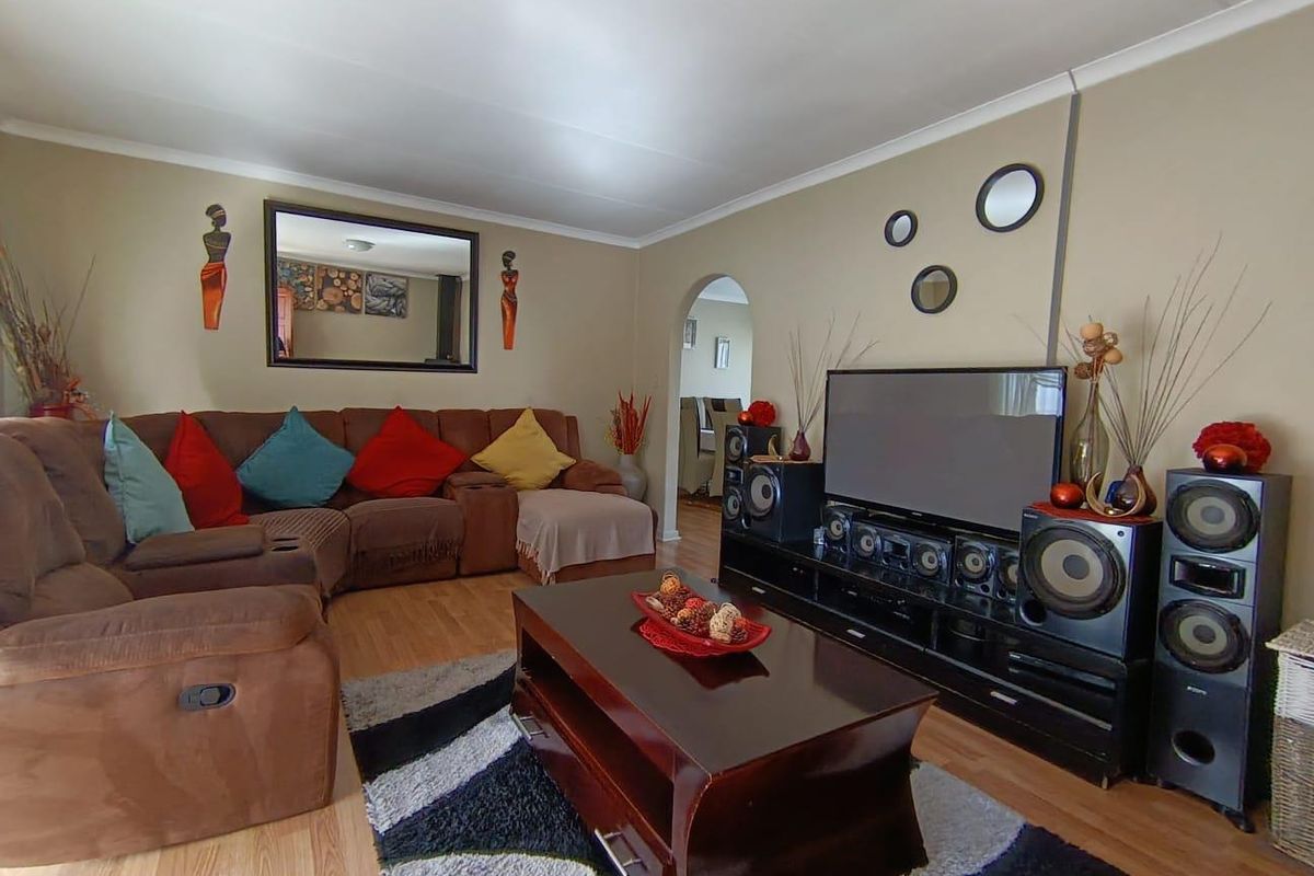 A comfortable living room featuring laminate flooring, coved ceilings, and an arched doorway leading to adjacent living spaces.