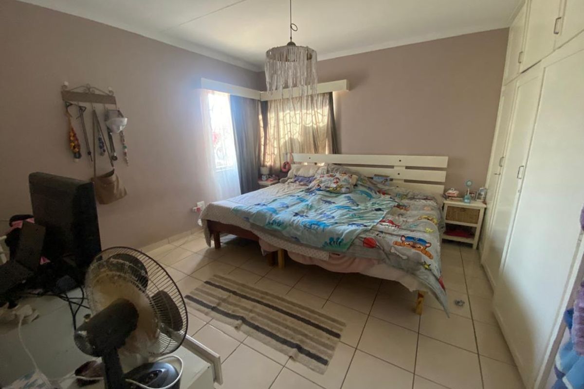 A bedroom featuring built-in cupboards, tiled flooring, and a window with curtaining.