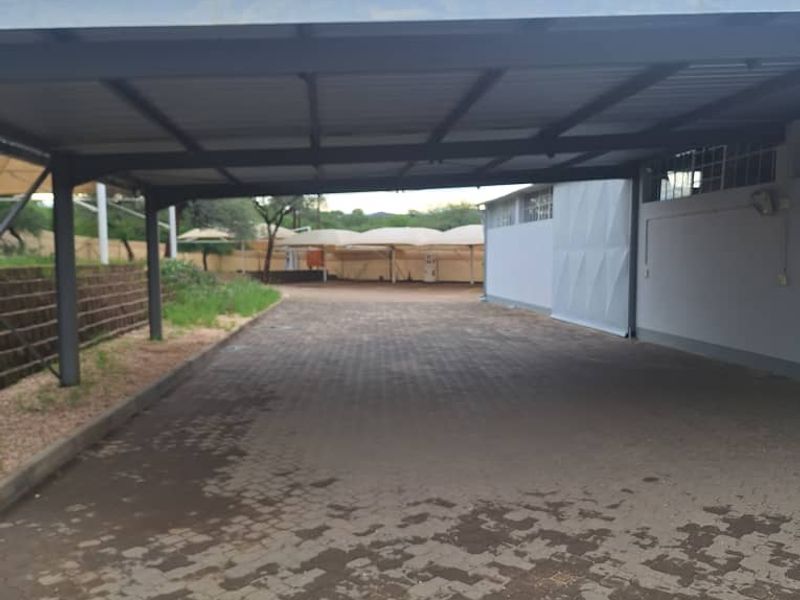 A spacious covered parking area featuring a metal roof structure and paved driveway, suitable for industrial or commercial vehicle storage.