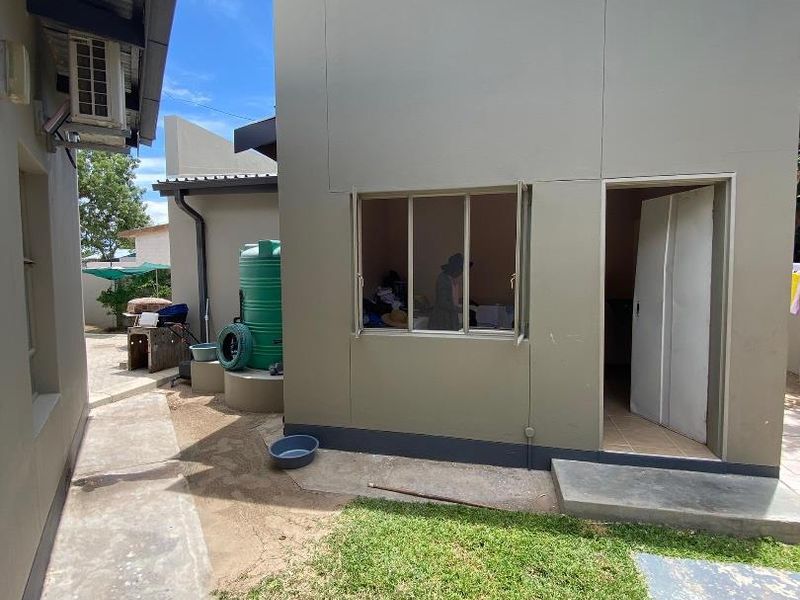 Rear exterior view of the property featuring a concrete pathway, water storage tank, and access to an external room with a casement window.