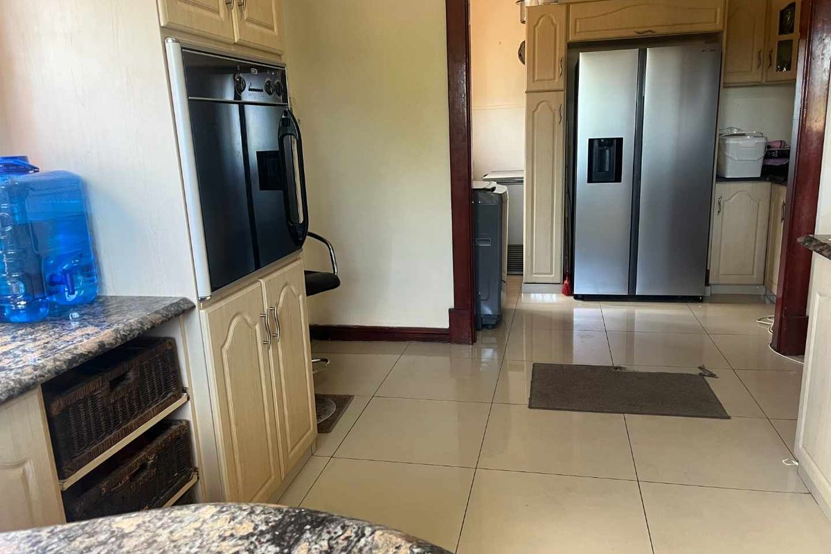 A functional kitchen area featuring light-toned cabinetry, built-in oven, and tiled flooring, with an adjacent scullery or utility space visible through the doorway.