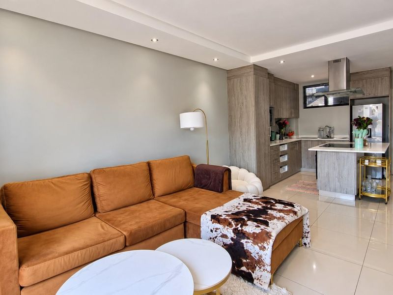 Modern open-plan living area featuring a contemporary kitchen with built-in cabinetry, an island, and recessed ceiling lighting, seamlessly connected to the lounge space.