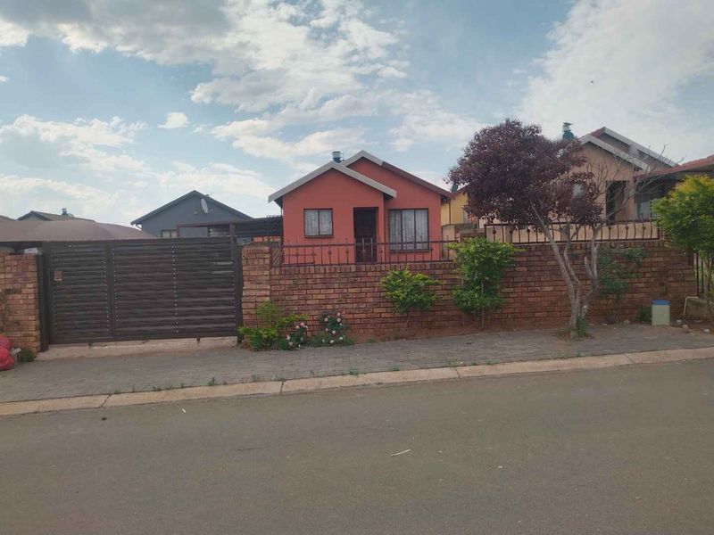 Front view of a detached house featuring a brick boundary wall, metal driveway gate, and a paved sidewalk area.
