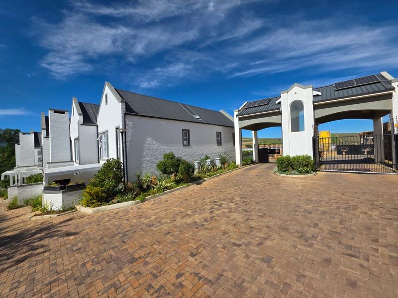 Front view of a modern townhouse complex featuring a brick paved driveway, secure gated entrance, and white painted brick architecture with solar panels.