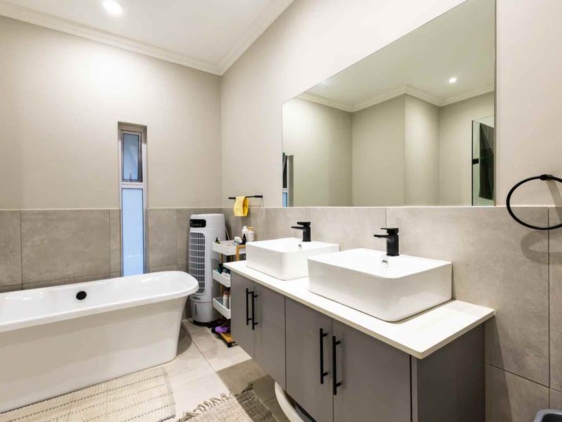 Modern bathroom featuring a sleek double vanity with vessel sinks, a large wall-to-wall mirror, and a contemporary freestanding bathtub.