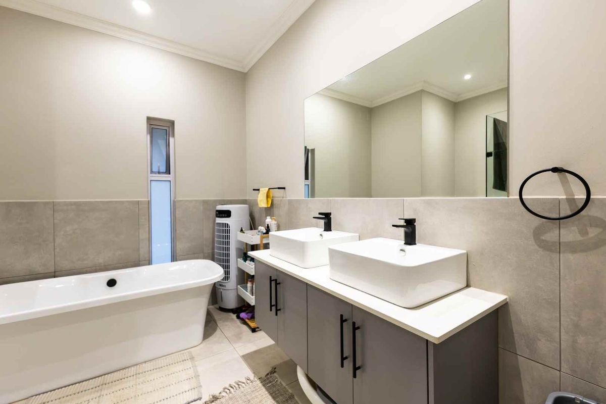 Modern bathroom featuring a sleek double vanity with vessel sinks, a large wall-to-wall mirror, and a contemporary freestanding bathtub.