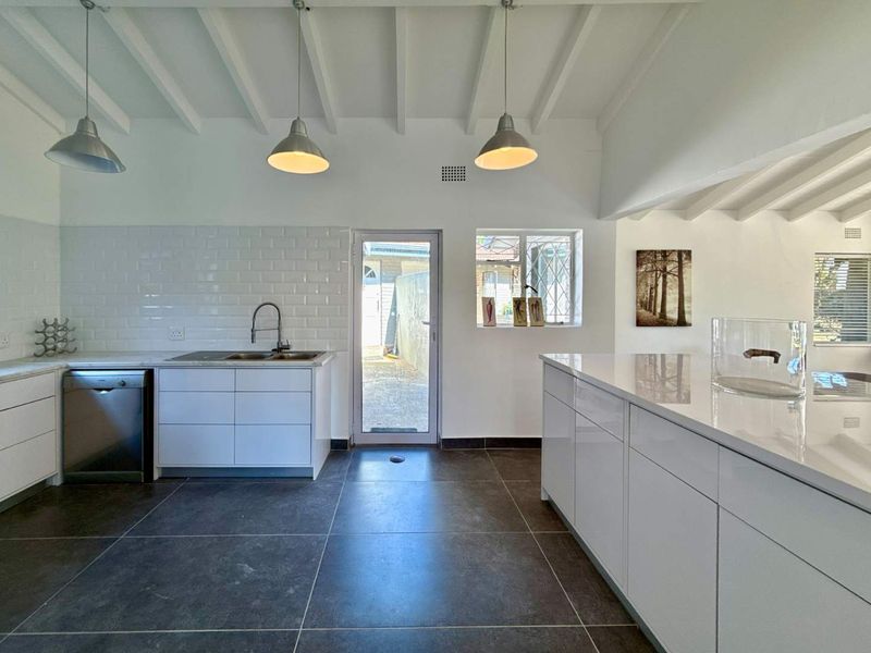 Modern kitchen featuring white cabinetry, stone countertops, subway tile backsplash, exposed beam ceilings, and a central island with pendant lighting.