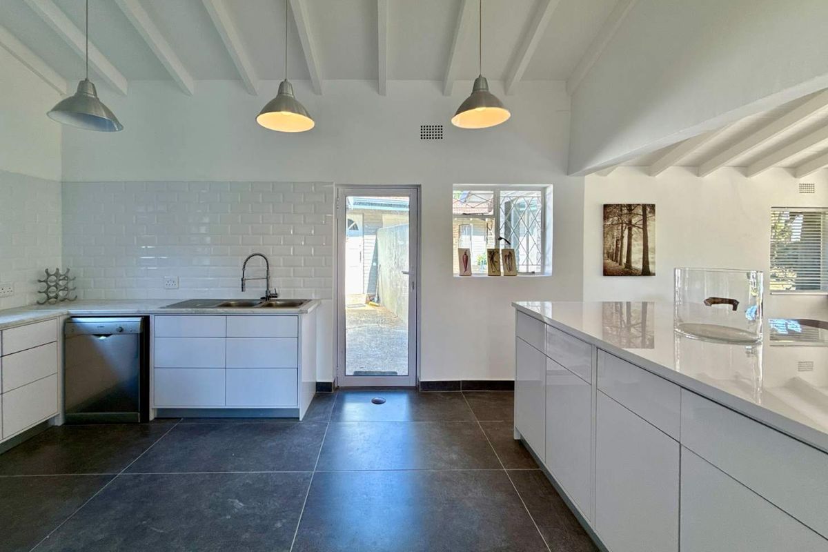 Modern kitchen featuring white cabinetry, stone countertops, subway tile backsplash, exposed beam ceilings, and a central island with pendant lighting.