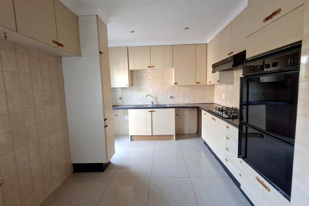 A functional kitchen featuring built-in cabinetry, a double wall oven, gas hob, extractor fan, and tiled finishes throughout.