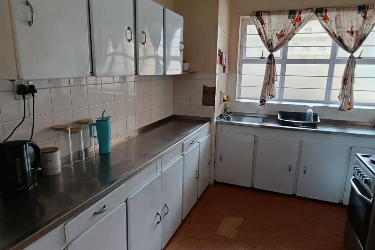 A functional kitchen featuring stainless steel countertops, built-in white cabinetry, a tiled backsplash, and a large window providing natural light.