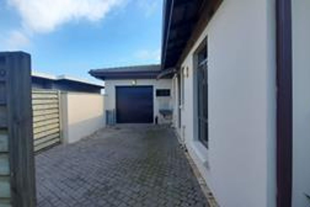 A side view of the property featuring a paved driveway leading to a garage, enclosed by boundary walls and timber fencing.