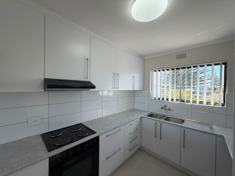 A clean, modern kitchen featuring white cabinetry, a built-in electric stove with extractor fan, double bowl sink, and neutral tiled splashback.