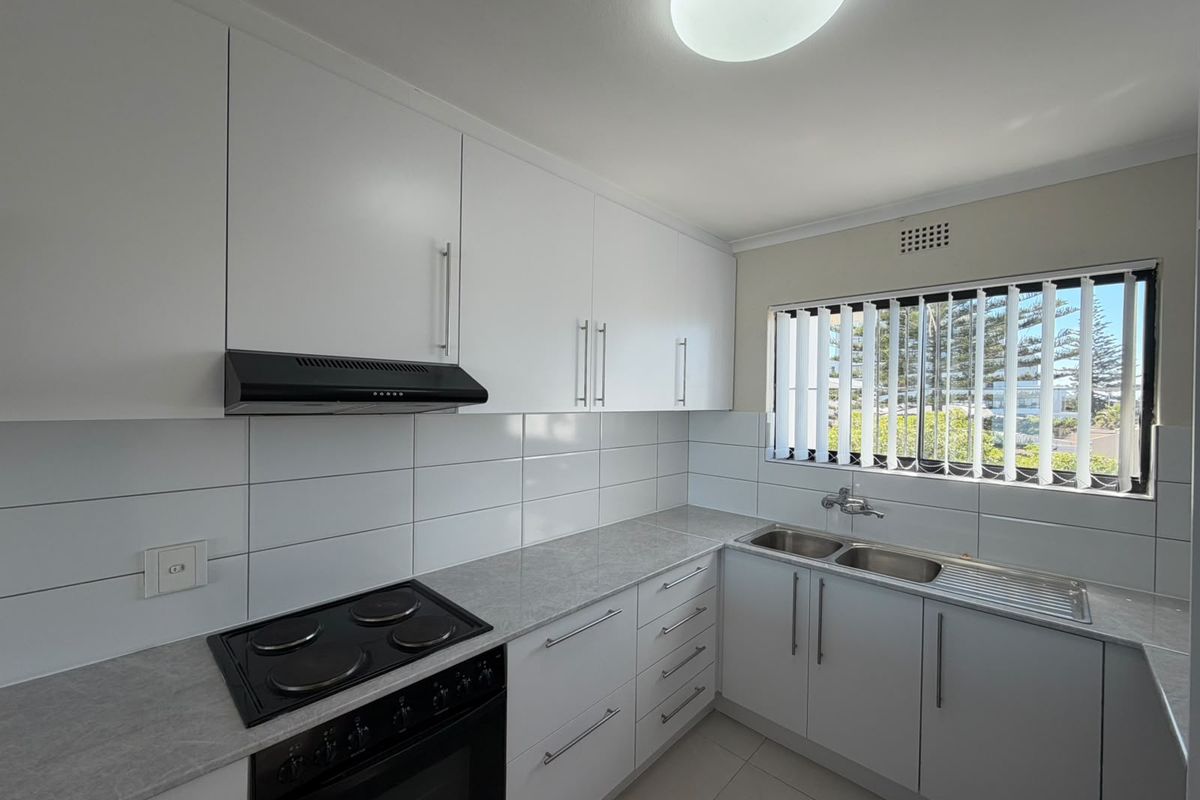 A clean, modern kitchen featuring white cabinetry, a built-in electric stove with extractor fan, double bowl sink, and neutral tiled splashback.