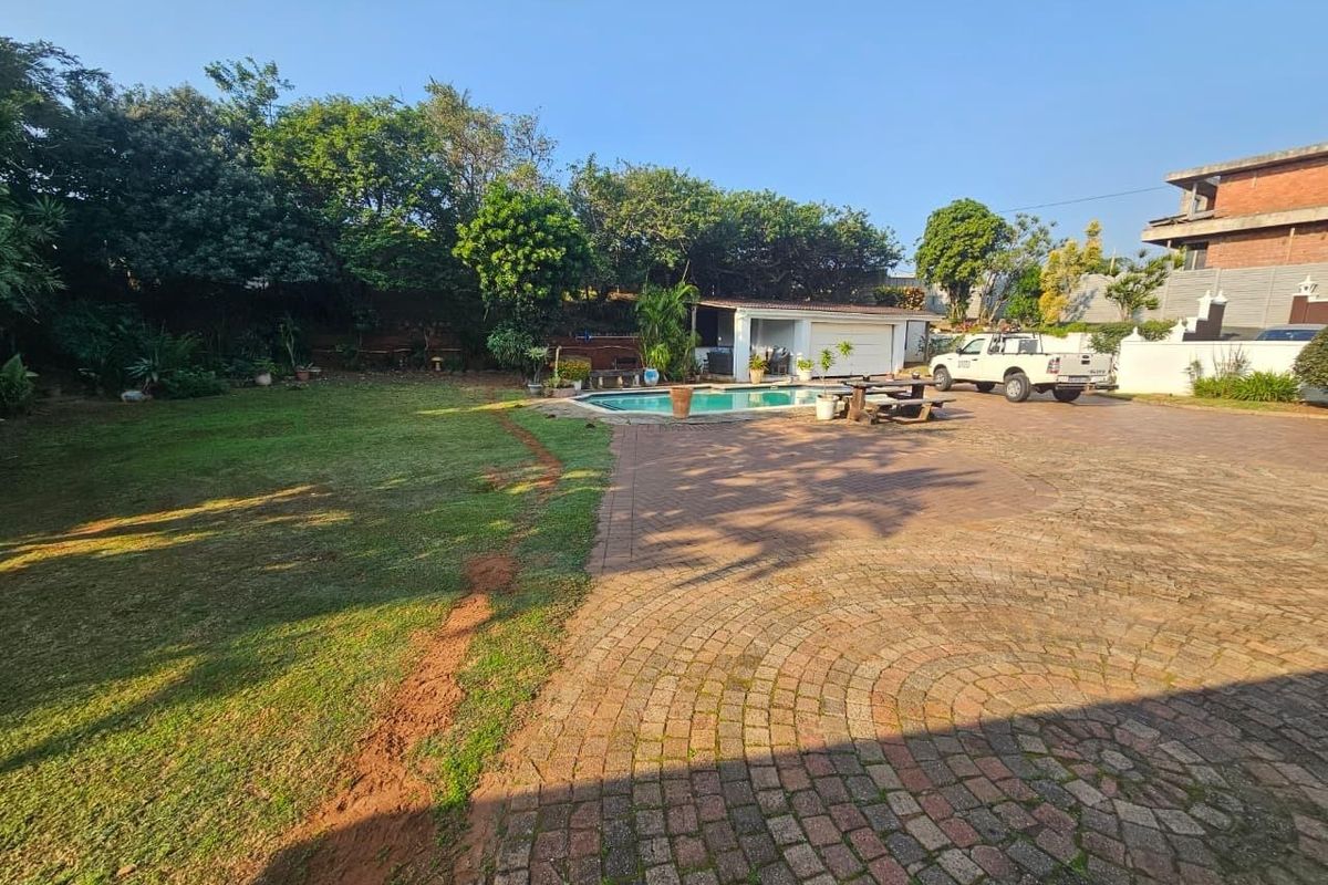 Spacious rear exterior featuring a paved driveway, swimming pool, and a large lawn area with established trees and a detached garage.