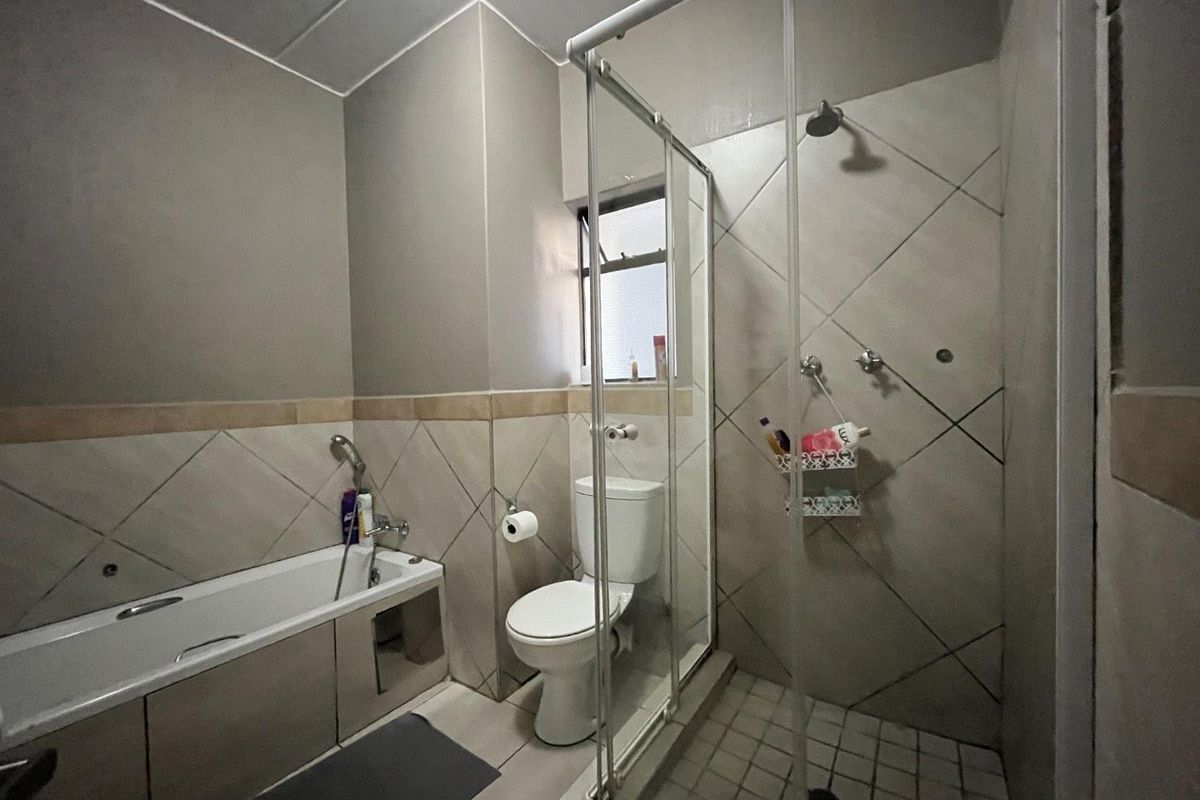 A functional bathroom featuring a built-in bathtub, a separate glass-enclosed shower, and neutral wall tiling.