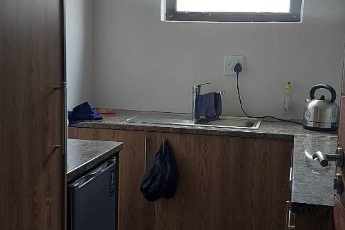 A compact kitchenette featuring wood-grain cabinetry, a stainless steel sink, and tiled flooring, suitable for office use.