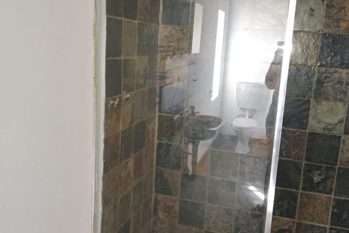 A bathroom featuring a walk-in shower with dark slate-style wall and floor tiles, complemented by a wooden ceiling and a separate toilet area.
