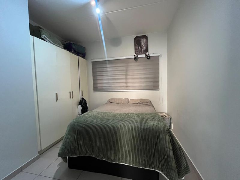 A functional bedroom featuring built-in wardrobes, tiled flooring, and a roller blind, providing a clean and practical living space.