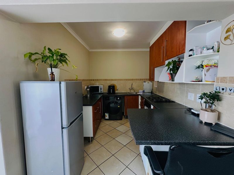 A functional kitchen featuring wooden cabinetry, dark laminate countertops, a tiled backsplash, and ceramic floor tiles with an integrated gas hob.