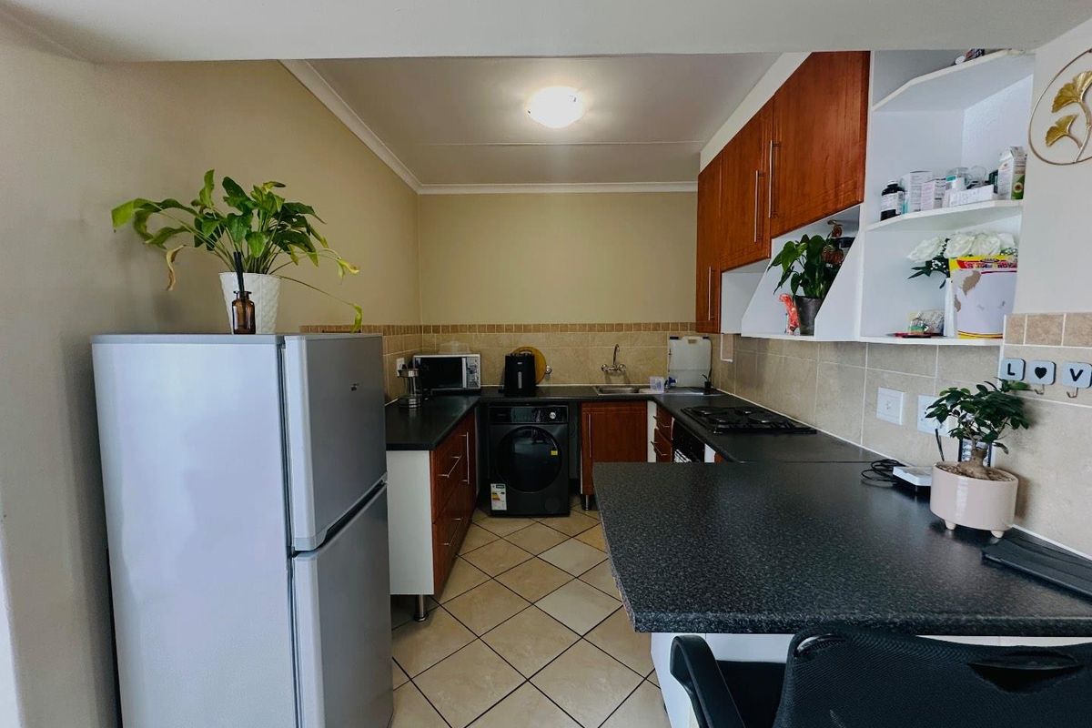 A functional kitchen featuring wooden cabinetry, dark laminate countertops, a tiled backsplash, and ceramic floor tiles with an integrated gas hob.