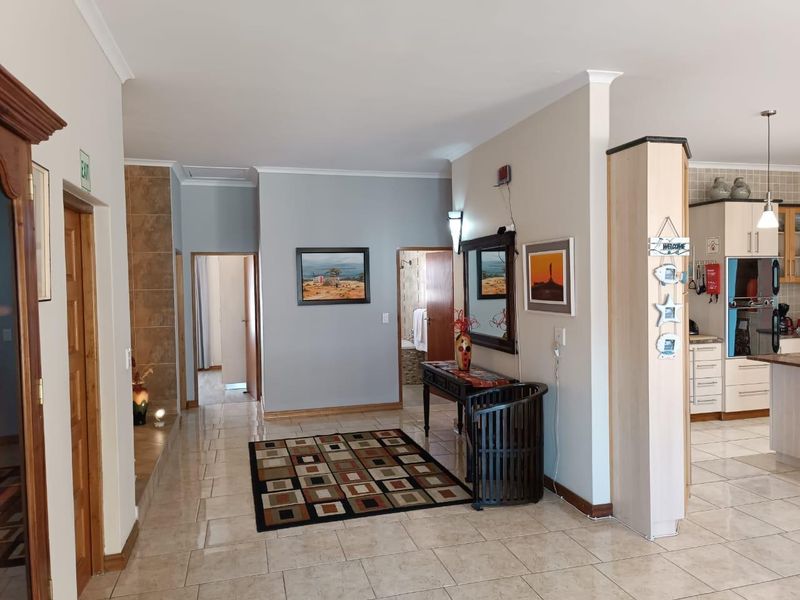 An open-plan living area featuring tiled flooring, coving, and a view into the adjacent kitchen with built-in cabinetry and appliances.