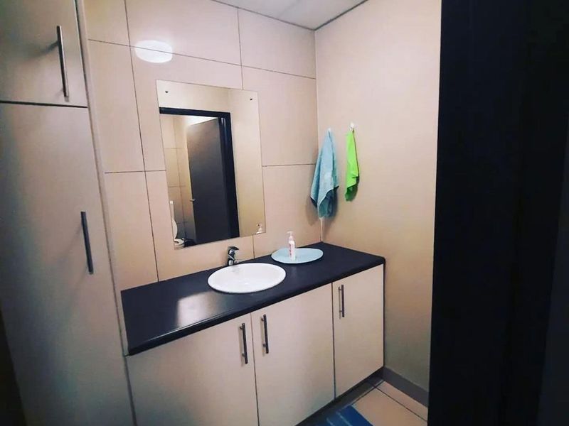 A functional bathroom featuring a vanity cabinet with a basin, countertop, wall mirror, and integrated storage cupboard with tiled wall finishes.