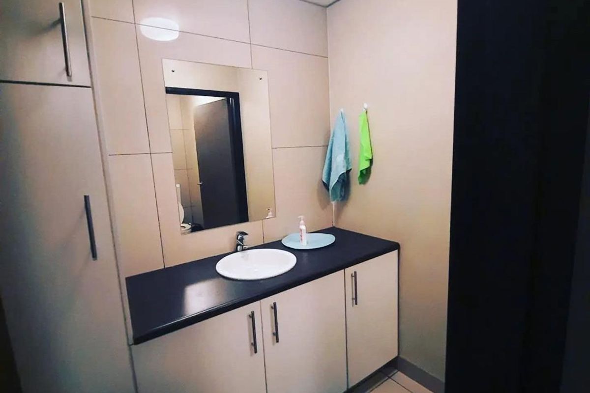 A functional bathroom featuring a vanity cabinet with a basin, countertop, wall mirror, and integrated storage cupboard with tiled wall finishes.