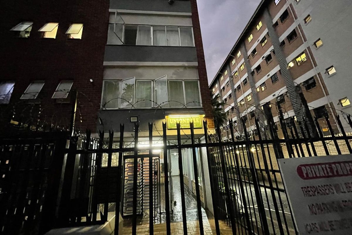 Exterior view of the apartment building entrance featuring secure gated access and multi-story brick facade architecture.