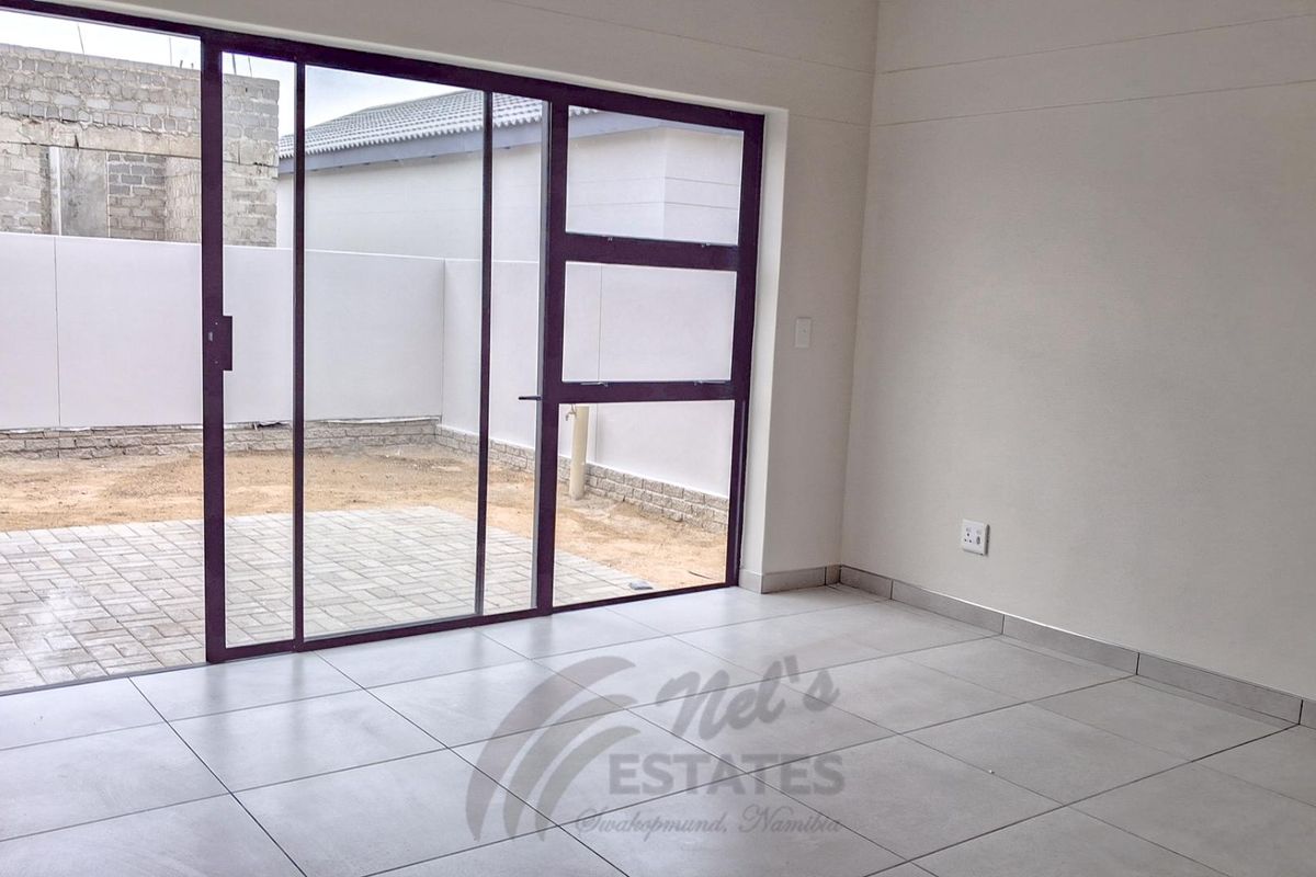 A bright, empty living area featuring large sliding glass doors that open onto a paved patio and private rear garden space.