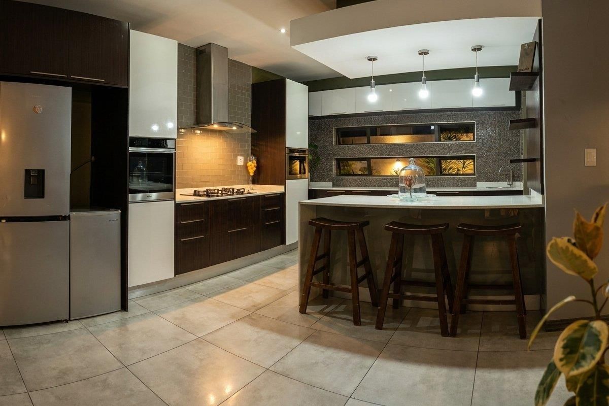 Modern kitchen featuring high-gloss cabinetry, stone countertops, a central island with breakfast bar, integrated appliances, and stylish tiled backsplash with feature lighting.