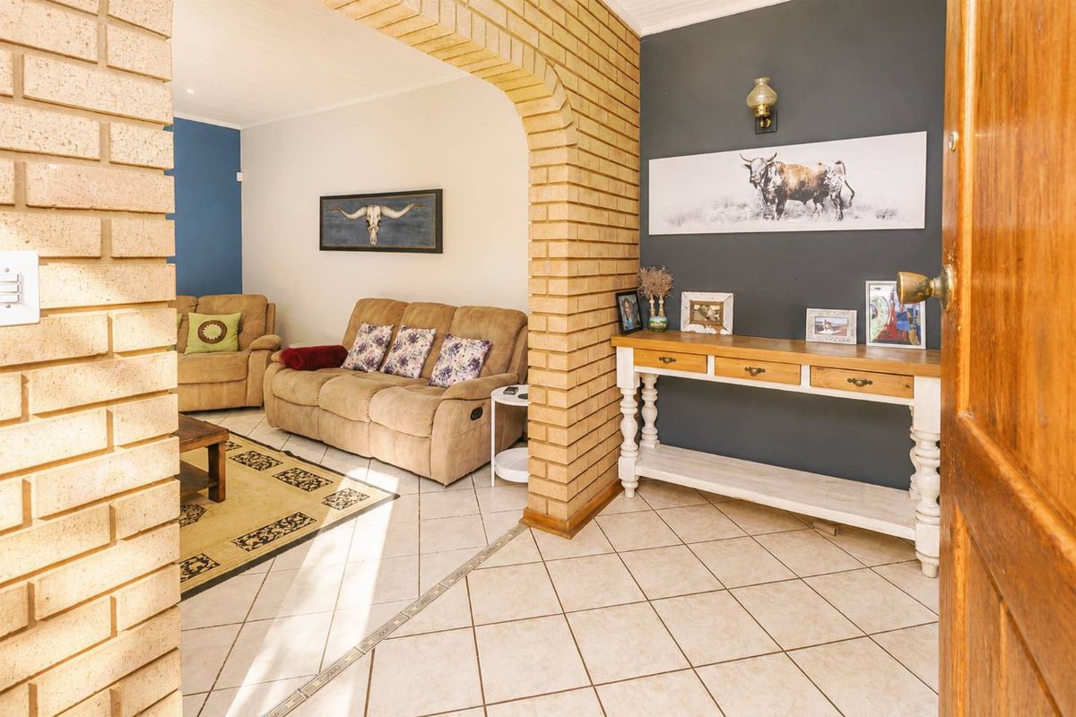 A living area featuring an exposed brick archway, tiled flooring, and a neutral color palette with a feature wall.